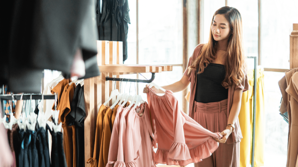 Attractive Asian woman browsing through a clothing store, carefully examining fashionable garments while shopping.