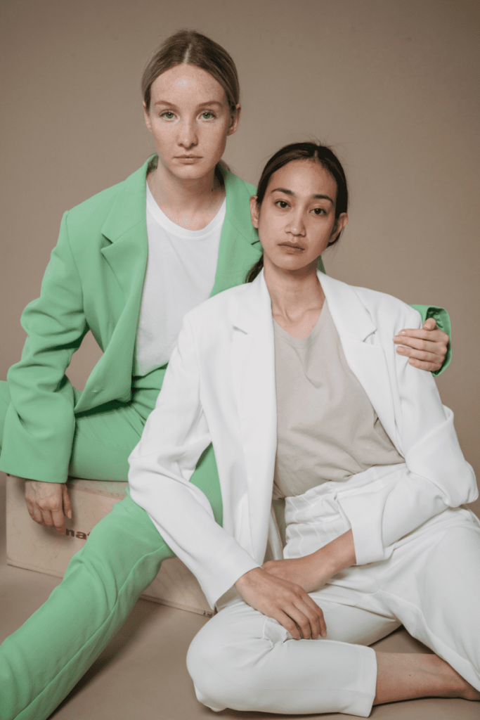 Two women wearing white and green professional attire striking a pose together.