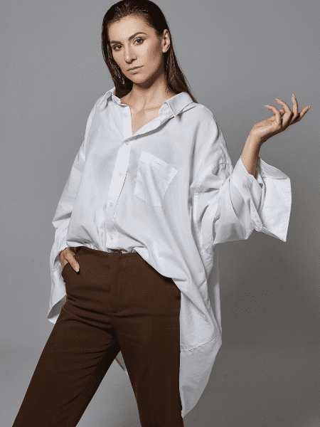 Confident young woman in trendy clothes gesturing with open hand against a white background, representing wardrobe essentials like a white shirt or dress.