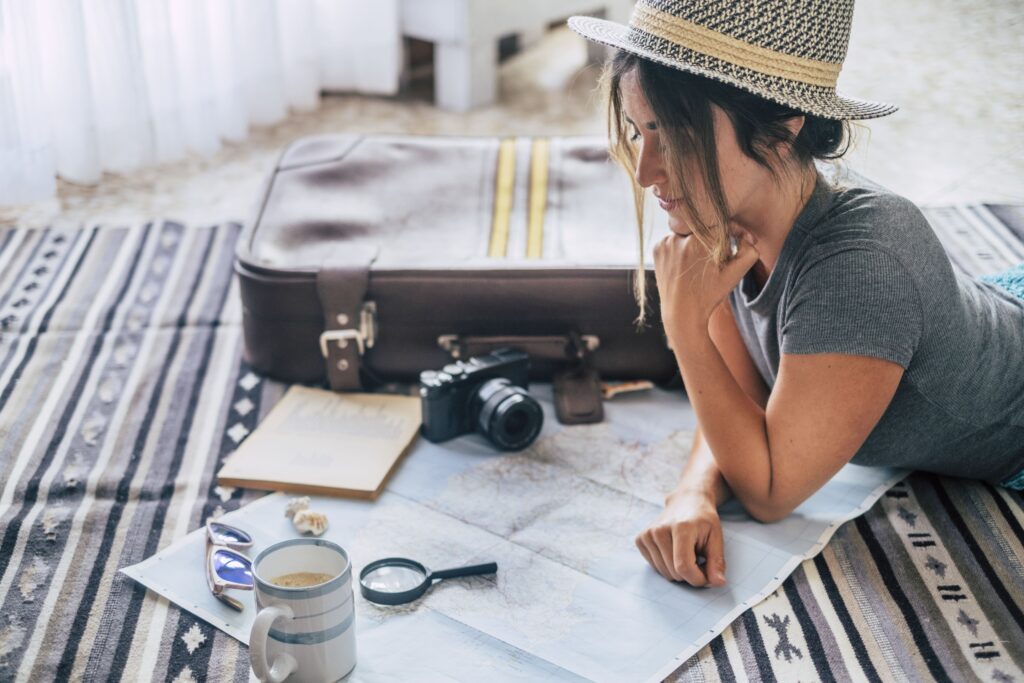 Caucasian woman planning her vacation at home using a map and guide, comfortably sitting on the floor while organizing her upcoming holiday