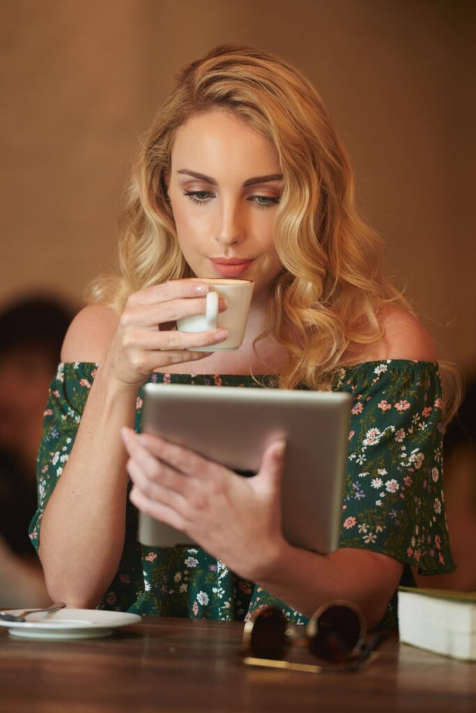 Free photo close up of blond woman browsing the web on the digital pad while drinking coffee in a cafe