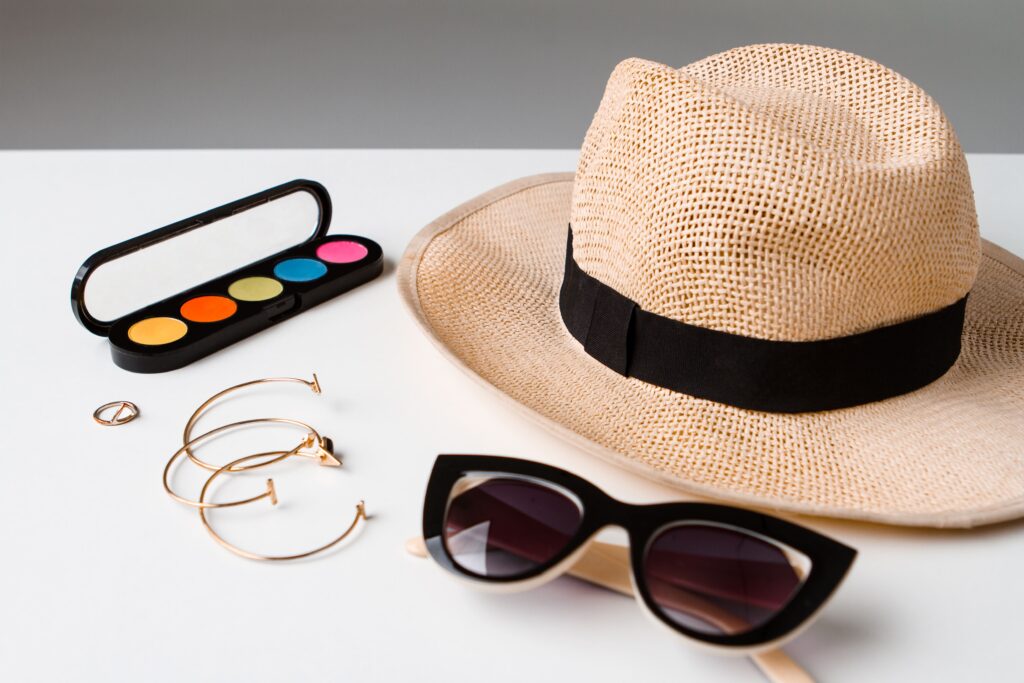 Decorative cosmetics, accessories, sunglasses, and hat displayed on a white table
