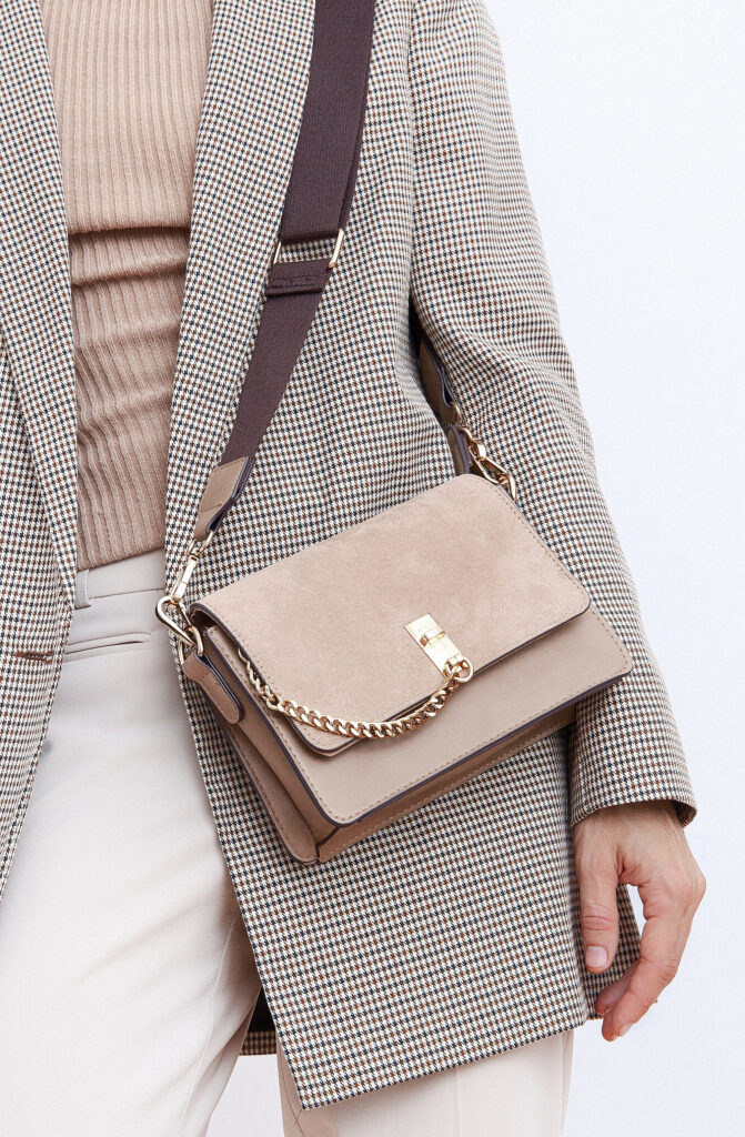 Details of a stylish Parisian woman's daily outfit, featuring a casual beige checkered jacket, velvet bag, and minimalistic accessories for a trendy look in fall, winter, and spring seasons.