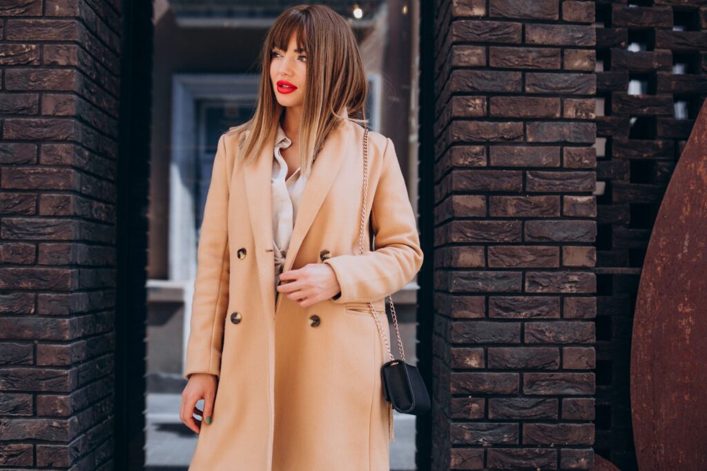 Complimentary image of a stylish young woman wearing a beige coat while posing outdoors.
