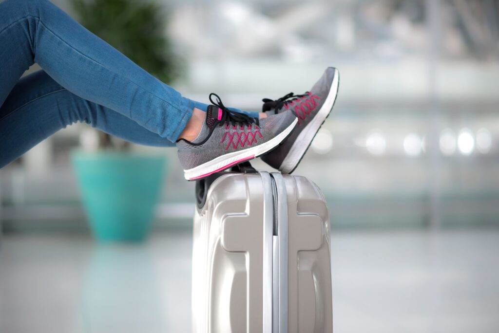 A photograph capturing a passenger's leg resting on luggage at the airport, showcasing their choice of footwear.