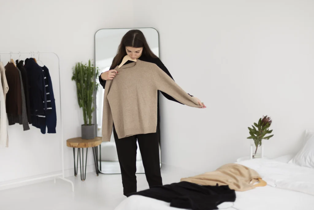 Full-length view of a woman thoughtfully holding a shirt, contemplating her clothing choices as she embraces a minimalist wardrobe approach.