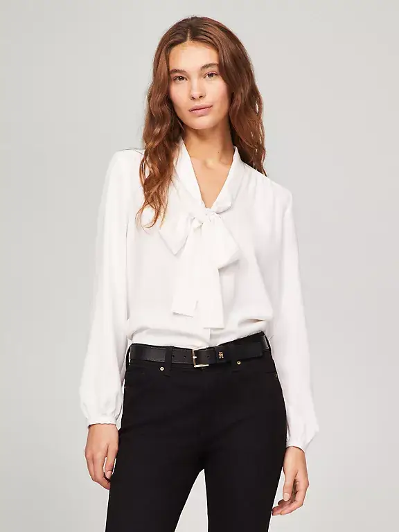 Elegant white tie-neck blouse styled with black high-waisted trousers for a sophisticated, timeless look suitable for work or formal settings.