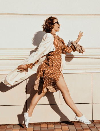 Timeless pieces accentuate a well-dressed girl with dark hair as she dashes down the street; an outdoor capture of an incredible female model showcasing her coat and white shoes.