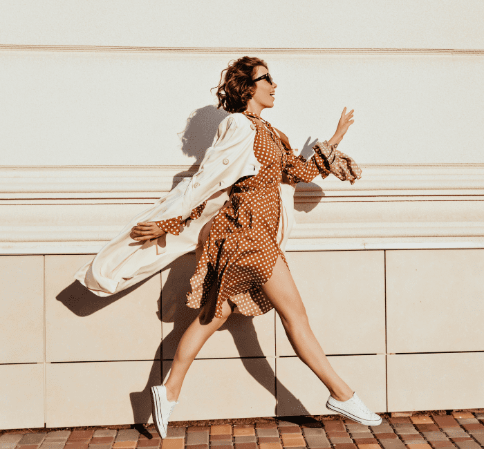 Timeless pieces accentuate a well-dressed girl with dark hair as she dashes down the street; an outdoor capture of an incredible female model showcasing her coat and white shoes.