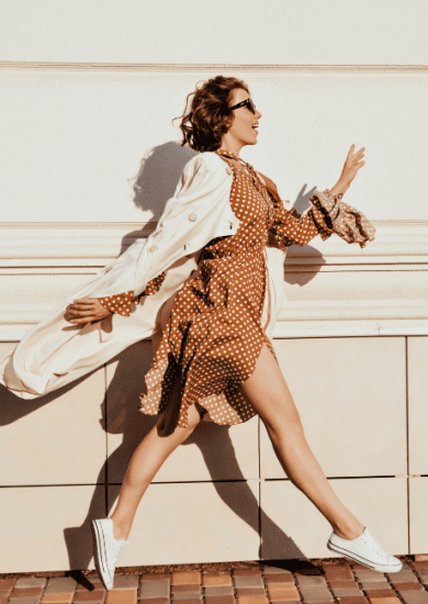Timeless pieces accentuate a well-dressed girl with dark hair as she dashes down the street; an outdoor capture of an incredible female model showcasing her coat and white shoes.