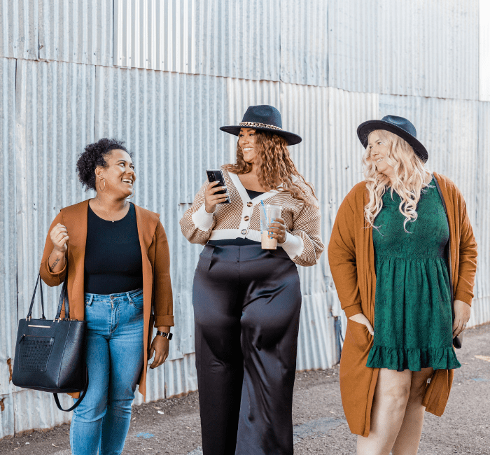 Group of women of different sizes, showcasing how to dress for your body type, wearing stylish bikinis and standing together against a brown background. Diverse women in swimwear looking at camera and smiling.