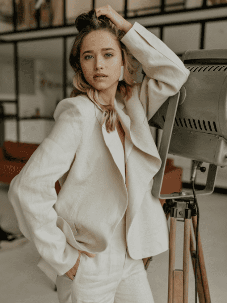 A photo of a blonde woman wearing a stylish linen suit leaning on a modern floor lamp, with a curly-haired woman wearing beige pants and a jacket next to her.