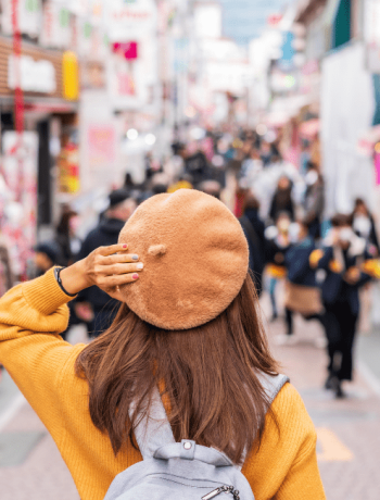 Young woman traveler in versatile clothing for travel, exploring Harajuku's Takeshita Street, the center of teenage fashion and cosplay culture in Tokyo