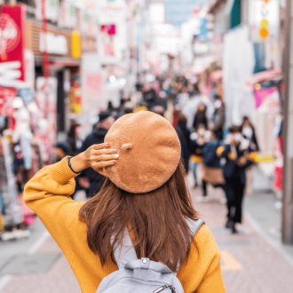 Young woman traveler in versatile clothing for travel, exploring Harajuku's Takeshita Street, the center of teenage fashion and cosplay culture in Tokyo