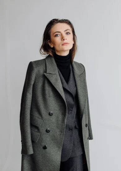 A woman embodying minimalist style, dressed in a black turtleneck, dark gray suit, and lighter gray jacket, demonstrating the art of color coordination and simplicity in fashion. Her ensemble reflects a monochromatic color palette, typical of a minimalist wardrobe, underlining the principles of sustainable and conscious fashion.