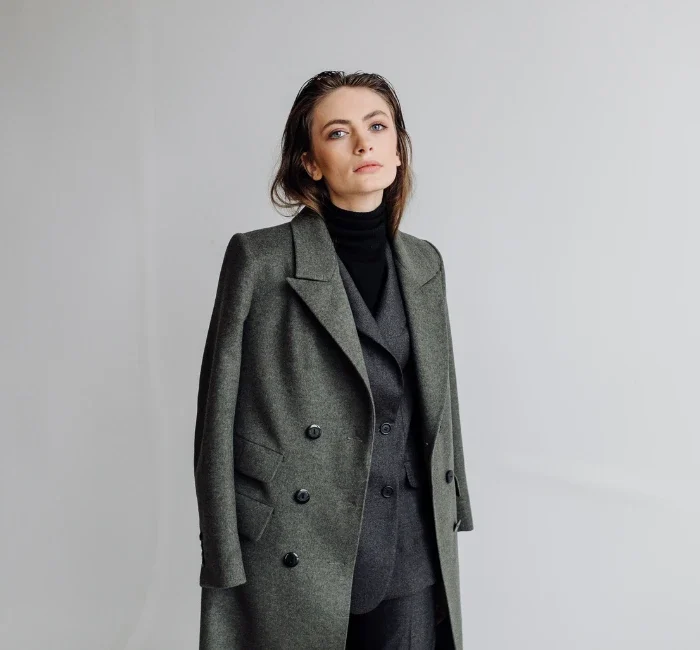 A woman embodying minimalist style, dressed in a black turtleneck, dark gray suit, and lighter gray jacket, demonstrating the art of color coordination and simplicity in fashion. Her ensemble reflects a monochromatic color palette, typical of a minimalist wardrobe, underlining the principles of sustainable and conscious fashion.