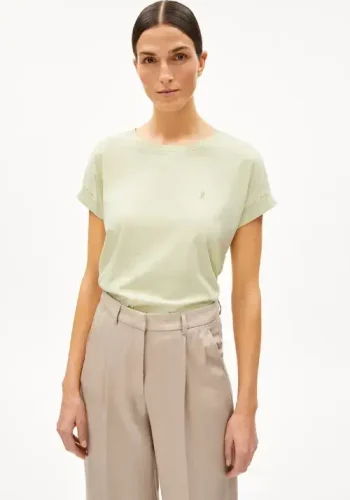 A woman wearing a light green short-sleeve t-shirt and beige high-waisted trousers poses confidently against a plain white background.