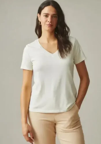 A woman wearing a white v-neck short-sleeve t-shirt and beige pants stands with a relaxed posture against a neutral background, exuding casual elegance.