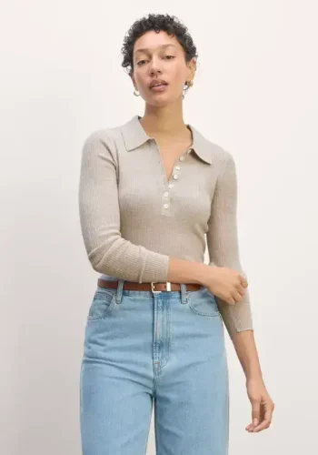 A woman wearing a beige ribbed collared top with button details and light blue high-waisted jeans poses confidently against a light neutral background.