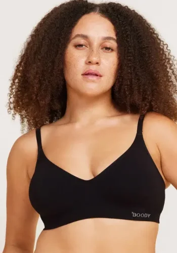 A woman with curly hair confidently models a black wireless t-shirt bra against a light background, showcasing body positivity and comfortable lingerie.