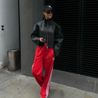 Lady showcasing her athleisure workplace dos and don'ts outfits with a black hat, black leather jacket, t shirt, and a red sports trousers, with white sneakers