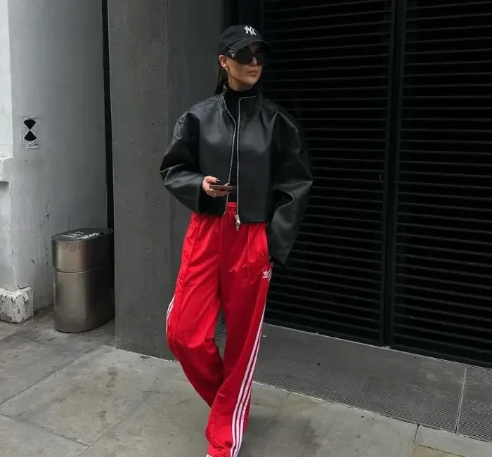 Lady showcasing her athleisure workplace dos and don'ts outfits with a black hat, black leather jacket, t shirt, and a red sports trousers, with white sneakers