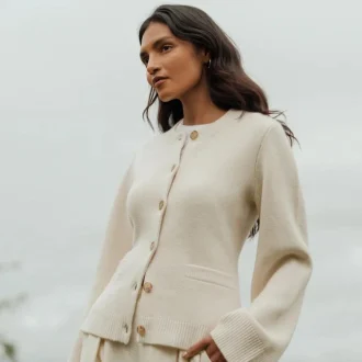 A woman poses elegantly in a neutral-colored Cooper Cardigan, a classic piece from one of the leading minimalist fashion brands.