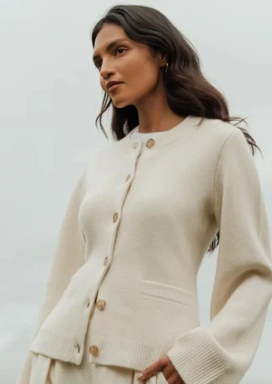 A woman poses elegantly in a neutral-colored Cooper Cardigan, a classic piece from one of the leading minimalist fashion brands.