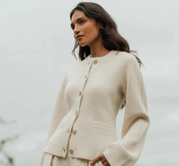 A woman poses elegantly in a neutral-colored Cooper Cardigan, a classic piece from one of the leading minimalist fashion brands.