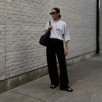 Minimalist style influencer Natalie Helen pulling off a casual dress code outfit wearing a darb pants with gray shirt, sunglasses, tote bag and slippers