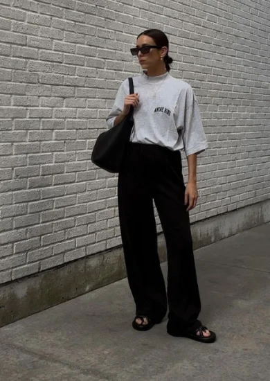 Minimalist style influencer Natalie Helen pulling off a casual dress code outfit wearing a darb pants with gray shirt, sunglasses, tote bag and slippers