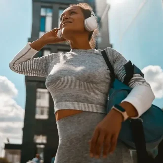 A woman wearing headphones and sporting her athleisure wear from budget-friendly fashion brands, smiling in the middle of town.