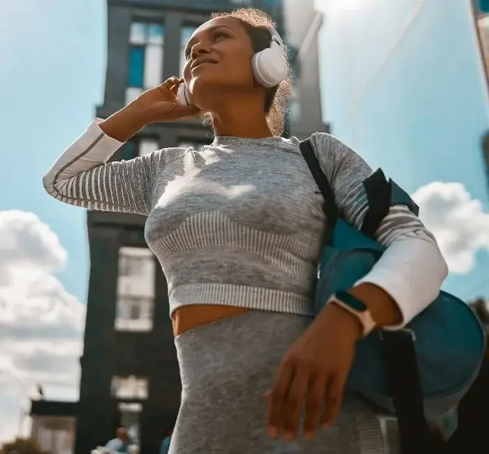 A woman wearing headphones and sporting her athleisure wear from budget-friendly fashion brands, smiling in the middle of town.