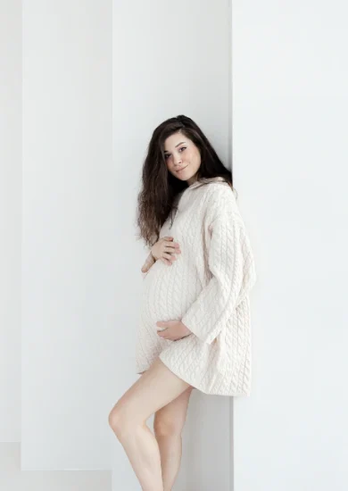 Expectant brunette woman showcasing maternity style in a comfortable oversized knitted sweater.