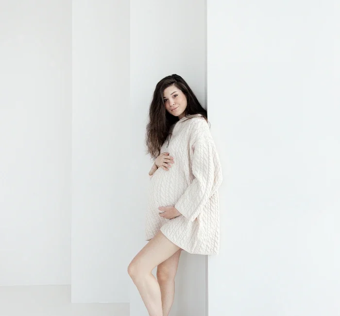 Expectant brunette woman showcasing maternity style in a comfortable oversized knitted sweater.