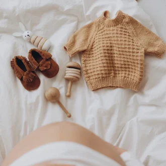 Top view of a pregnant woman's belly bump with stylish brown boho shoes, illustrating a maternity capsule wardrobe