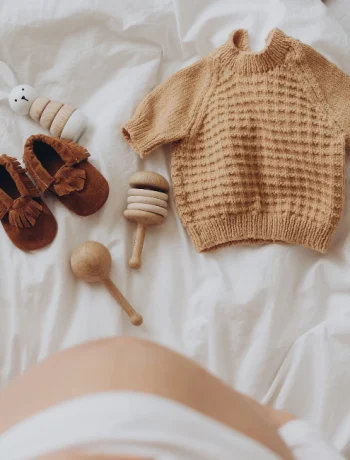 Top view of a pregnant woman's belly bump with stylish brown boho shoes, illustrating a maternity capsule wardrobe