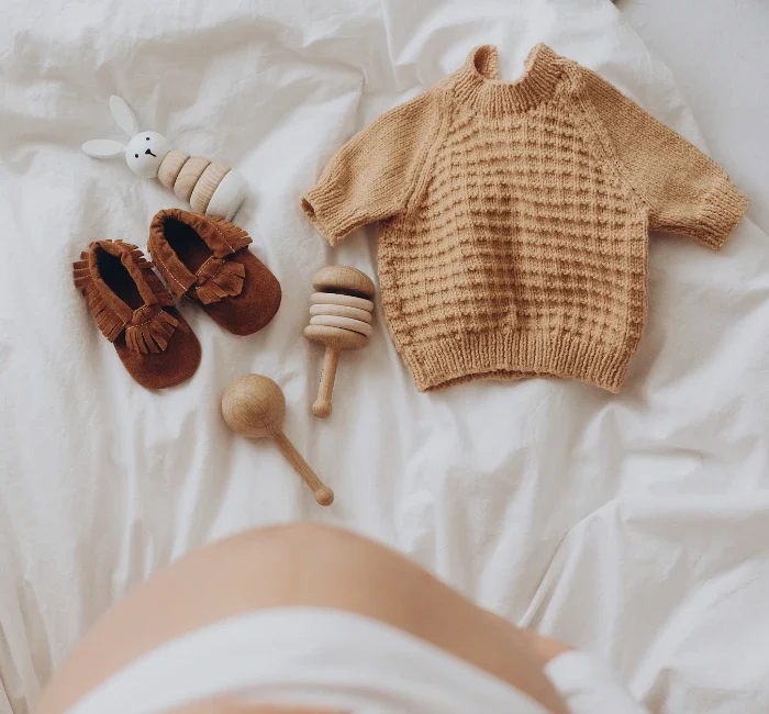 Top view of a pregnant woman's belly bump with stylish brown boho shoes, illustrating a maternity capsule wardrobe