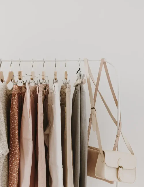 A minimalist clothing rack displaying neutral-toned pants and a beige handbag, highlighting a simple and cohesive fashion style.