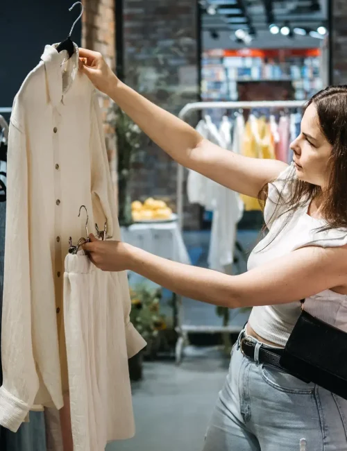 A woman carefully examining a beige shirt and matching pants in a clothing store, considering her style choices.