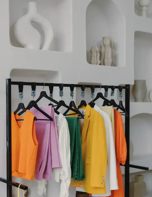 A clothing rack displaying vibrant, colorful garments including orange, yellow, green, and purple pieces, highlighting a bold and expressive fashion style.