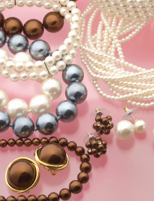 "An assortment of elegant pearl and bead necklaces and earrings arranged on a soft pink background, highlighting a collection of classic accessories.