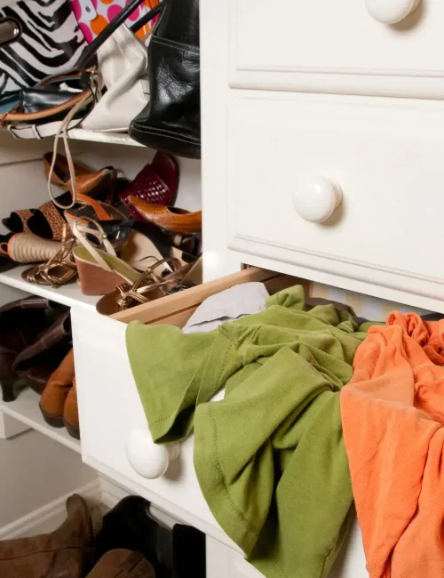 A cluttered drawer with clothes spilling out and a shelf filled with assorted shoes and bags, highlighting the need for wardrobe organization and decluttering.