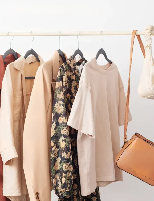 A minimalist clothing rack displaying neutral-toned garments and a tan handbag, showcasing a cohesive and stylish wardrobe collection.