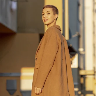 Lady with short hair smiling in a trench coat, looking at the sunrise – Minimalist Outerwear for fall.