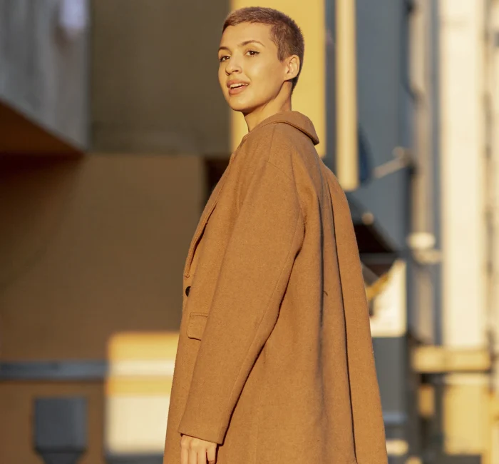 Lady with short hair smiling in a trench coat, looking at the sunrise – Minimalist Outerwear for fall.