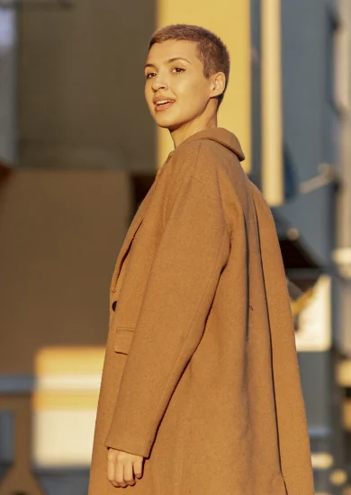 Lady with short hair smiling in a trench coat, looking at the sunrise – Minimalist Outerwear for fall.