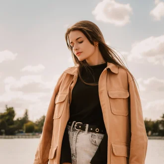 Photo of a caucasian young pretty stylish woman standing near river lake water street on sand pier showcasing Fall Minimalist Fashion