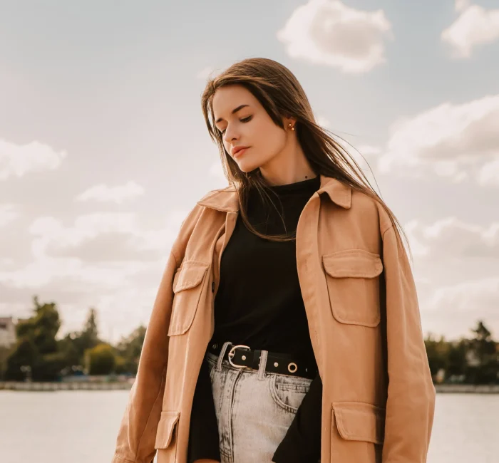 Photo of a caucasian young pretty stylish woman standing near river lake water street on sand pier showcasing Fall Minimalist Fashion