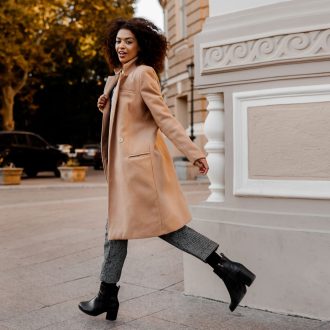 A full-length image of an elegant black woman in a luxurious beige coat and velvet sweater, showcasing a “budget fashion” style.